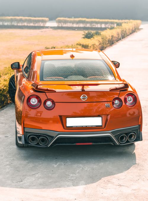 Free Captivating view of a shiny orange Nissan GTR with distinct tail lights, parked on a sunny day. Stock Photo