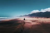 在西班牙帕哈拉广阔的沙滩上，一个孤独的人沿着海岸行走，背景是连绵的山脉