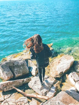 一个女人站在岩石海岸上，凝视着大海，她的头发在风中飘动