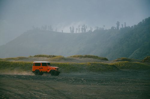 Free Orange SUV traversing a dirt road in the scenic mountains of East Java, Indonesia. Stock Photo