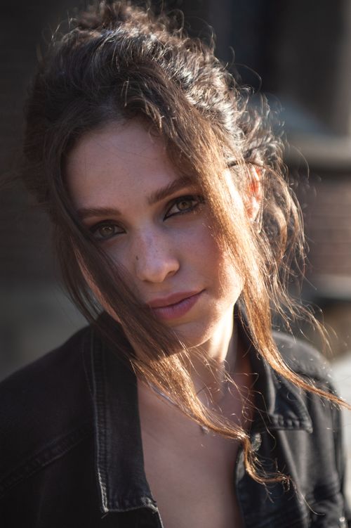 Free Captivating portrait of a young woman with brown hair in sunlight, wearing a denim jacket. Stock Photo
