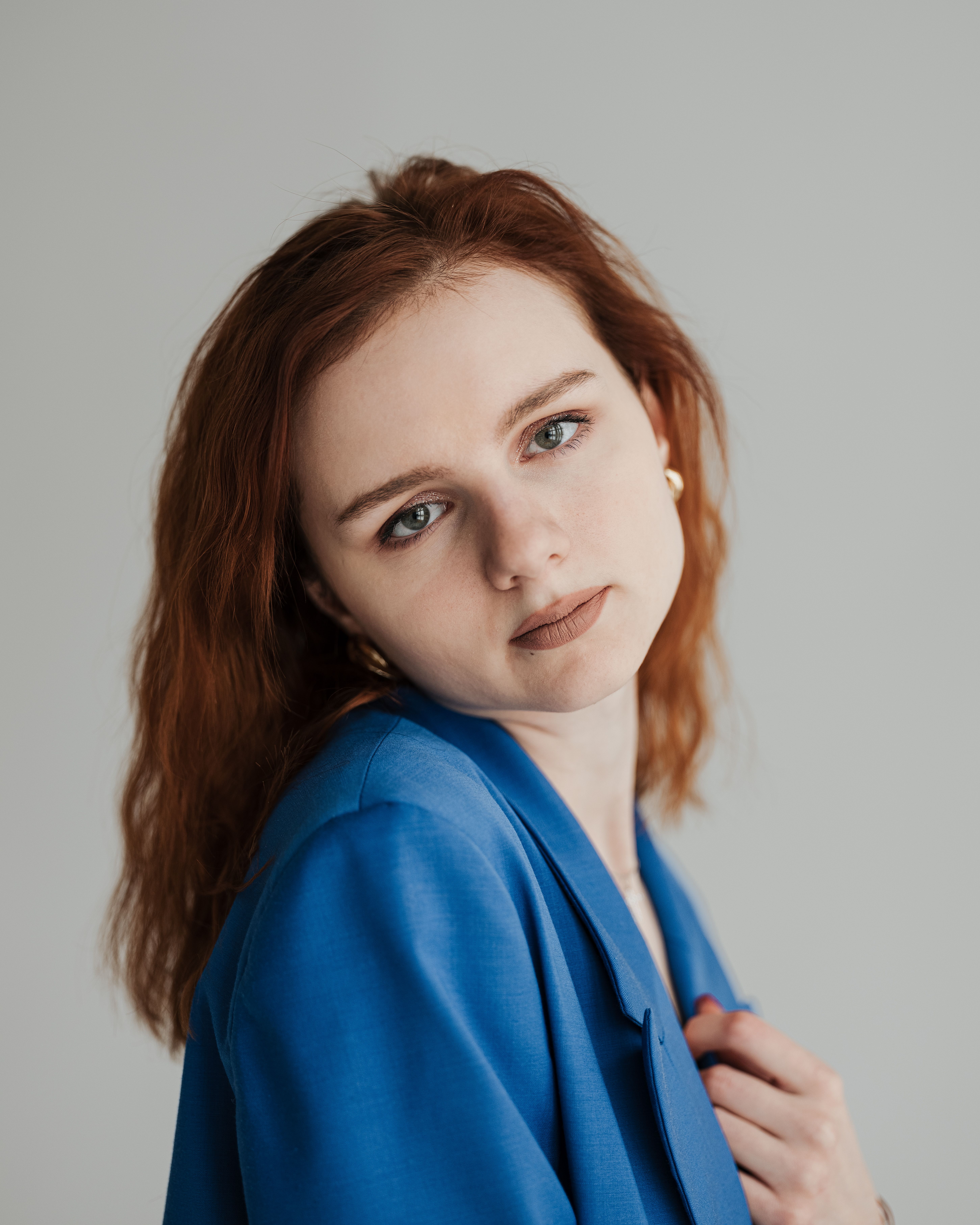 Studio portrait of a woman with red hair and blue blazer posing against a neutral background.
