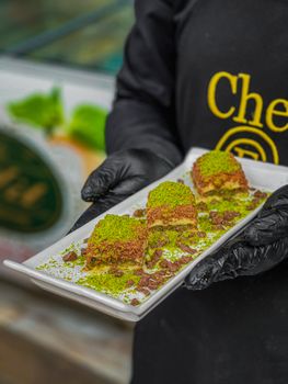 Close-up of a tasty pistachio dessert held on a plate by a person wearing gloves.
