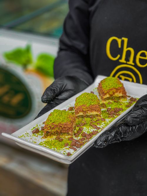 Free Close-up of a tasty pistachio dessert held on a plate by a person wearing gloves. Stock Photo