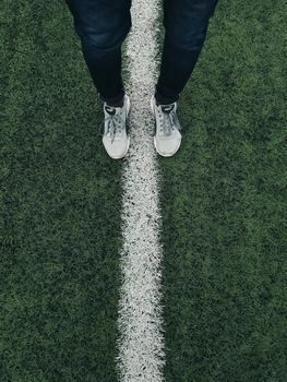 Top view of person standing on a grass field line, wearing jeans and sneakers.