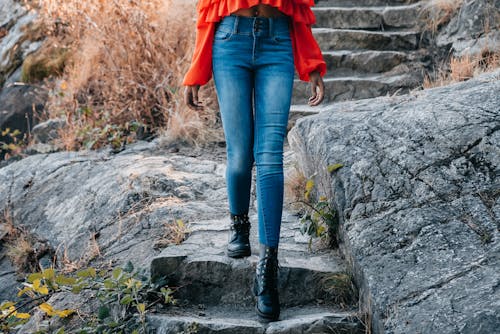 A Person in Denim Jeans and Black Leather Boots Walking Down the Rocky Stairs