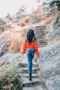 Woman in Orange Jacket and Blue Denim Jeans Standing on Rocky Ground