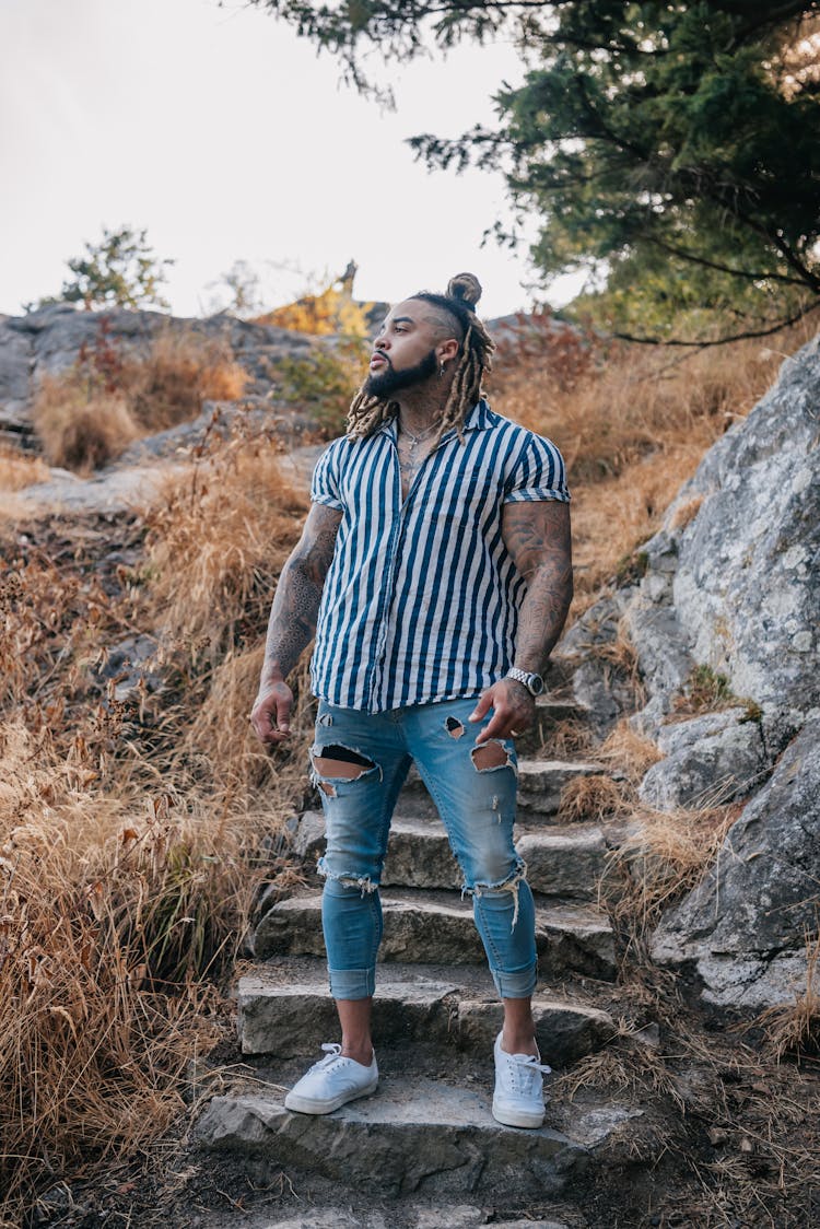 Man In Striped Polo And Ripped Jeans Standing On Stairs