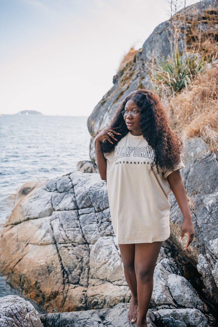 A Woman Wearing Oversized Shirt Standing On Big Rock While Looking Afar