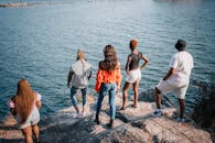 A Group of People Standing on Gray Rock Near Body of Water