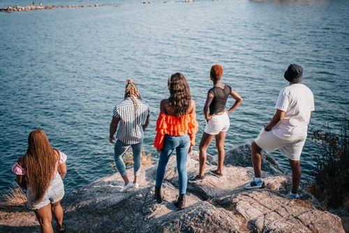 Free A group of friends stands on rocks overlooking a serene ocean, enjoying a sunny day. Stock Photo