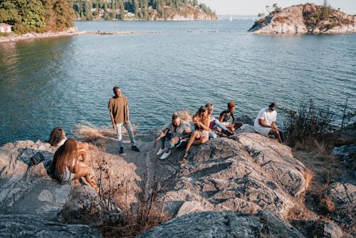 Free Group of People Sitting on Rock Formation Near Body of Water Stock Photo