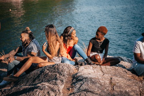 Group of People Sitting on Rock Near Body of Water