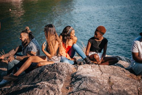 Free Group of friends enjoying a sunny day sitting by the lake on rocky shore. Stock Photo
