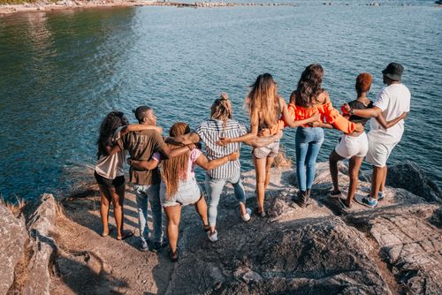 Free A group of friends standing on rocks, arms around each other, enjoying a scenic lake view. Stock Photo