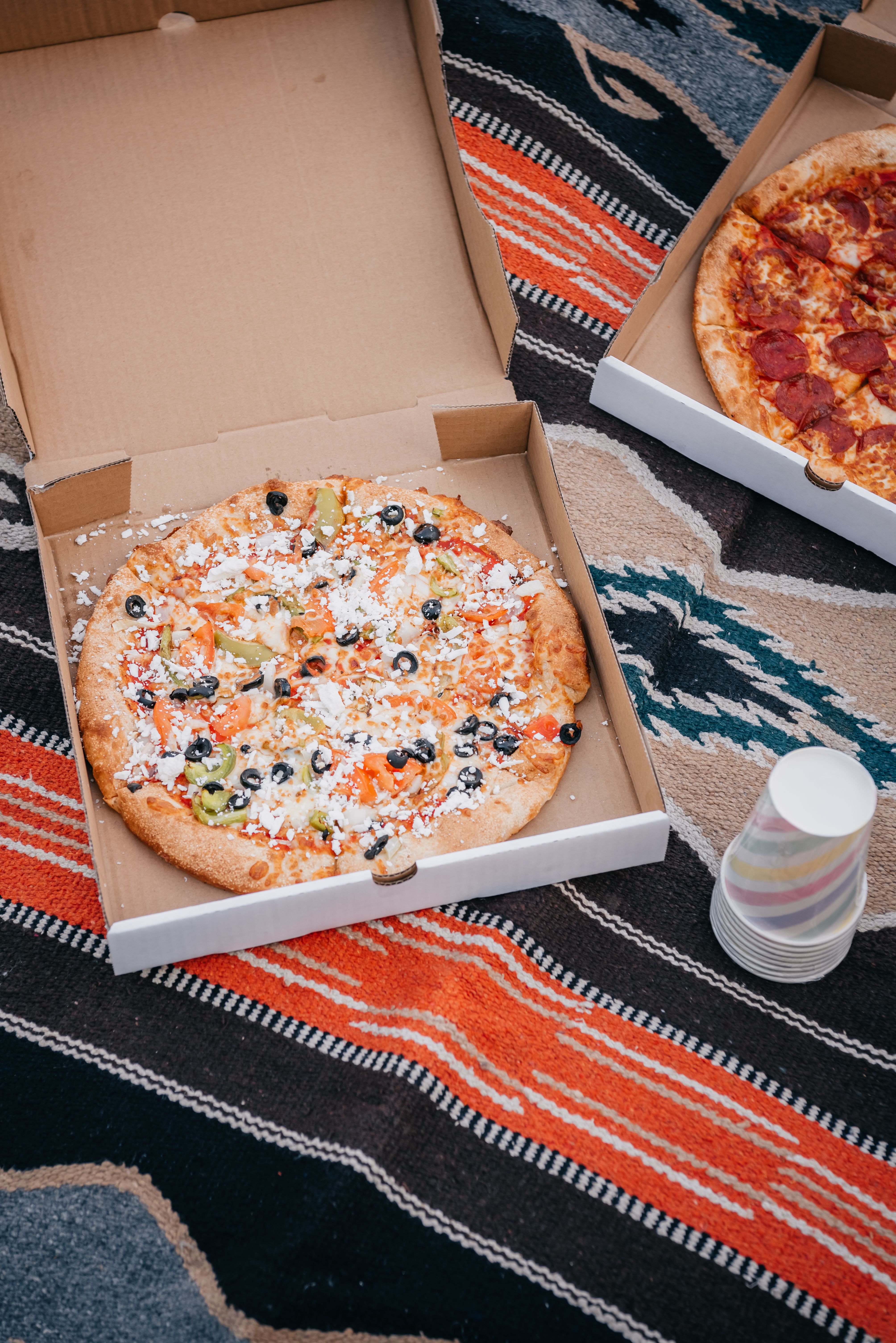 Delicious pizzas in takeout boxes on a vibrant blanket, perfect for a picnic setting.