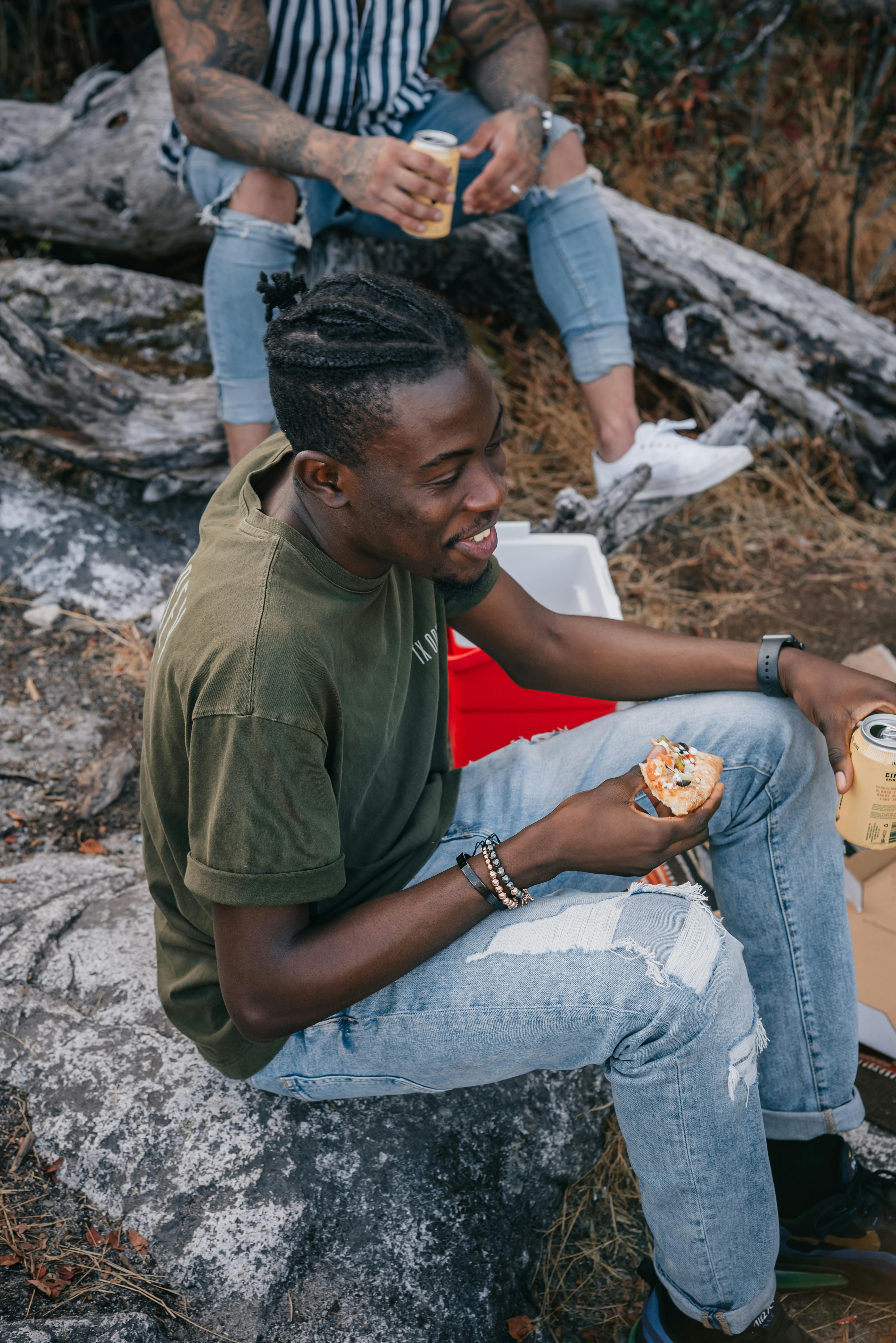 man in green shirt and blue denim jeans sitting on rock