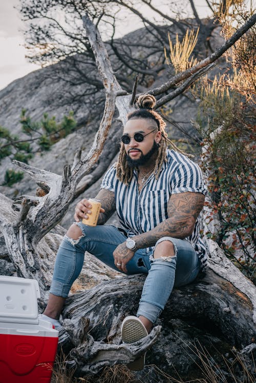 A Bearded Man Wearing Sunglasses Sitting on the Tree Log 