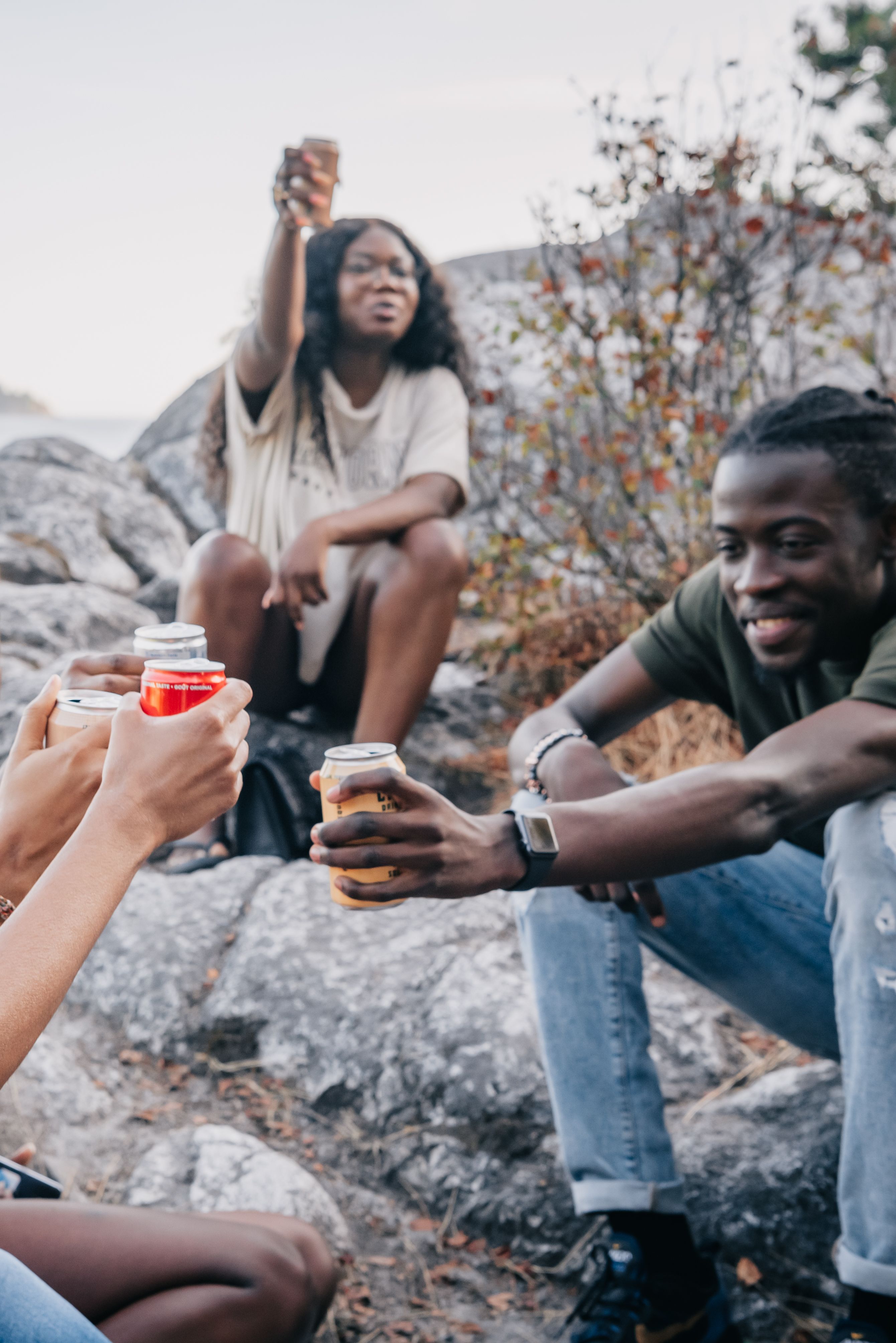 A group of friends enjoy drinks outdoors on a rocky area, toasting together.