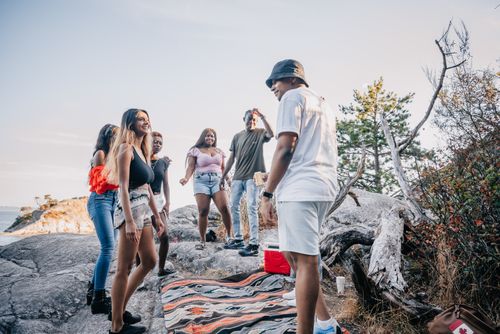 Free Diverse group of young adults laughing and socializing on rocks by the sea. Stock Photo