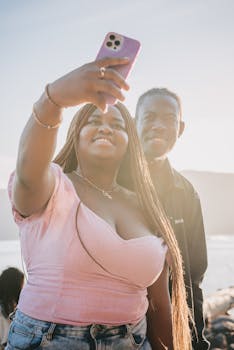 A joyful couple outdoors taking a selfie at sunset near the water.