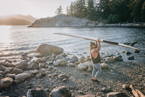 Free A man carrying a surfboard on a rocky beach during sunset, capturing a serene coastal scene. Stock Photo