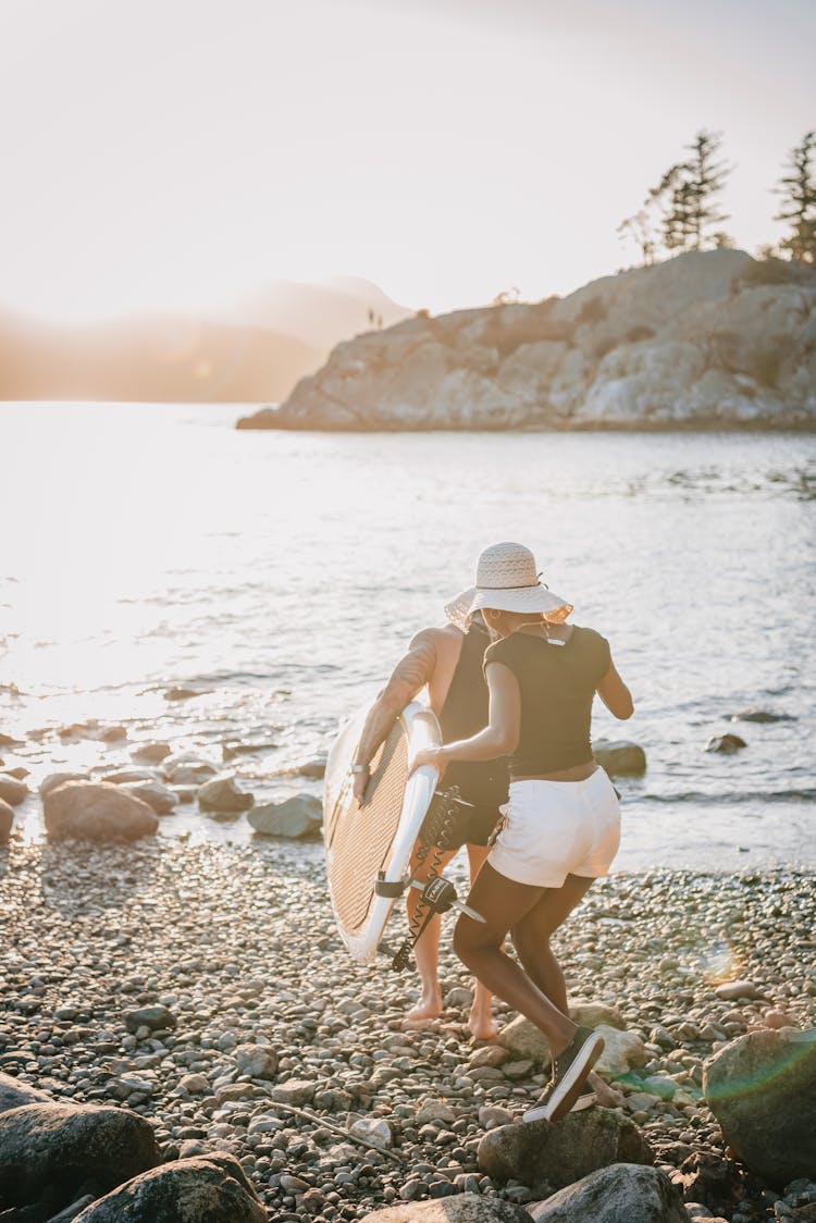 Couple With Surfboard Running Towards Water At Sunrise