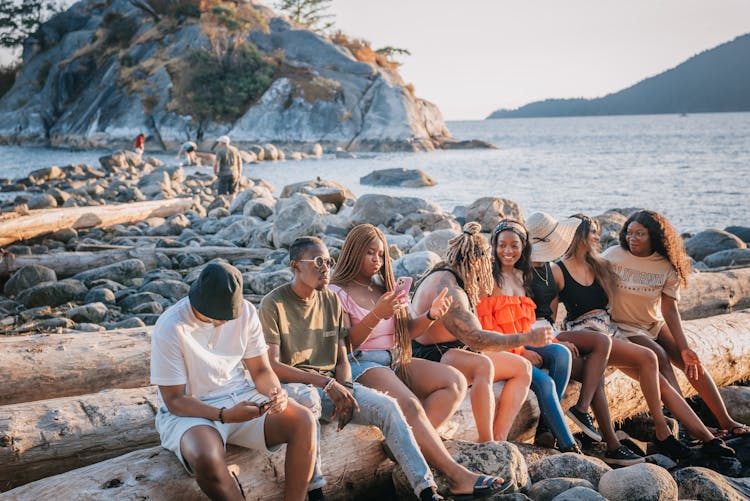 A Group Of Friends Sitting On Wood Log At The Beach While Having Conversation