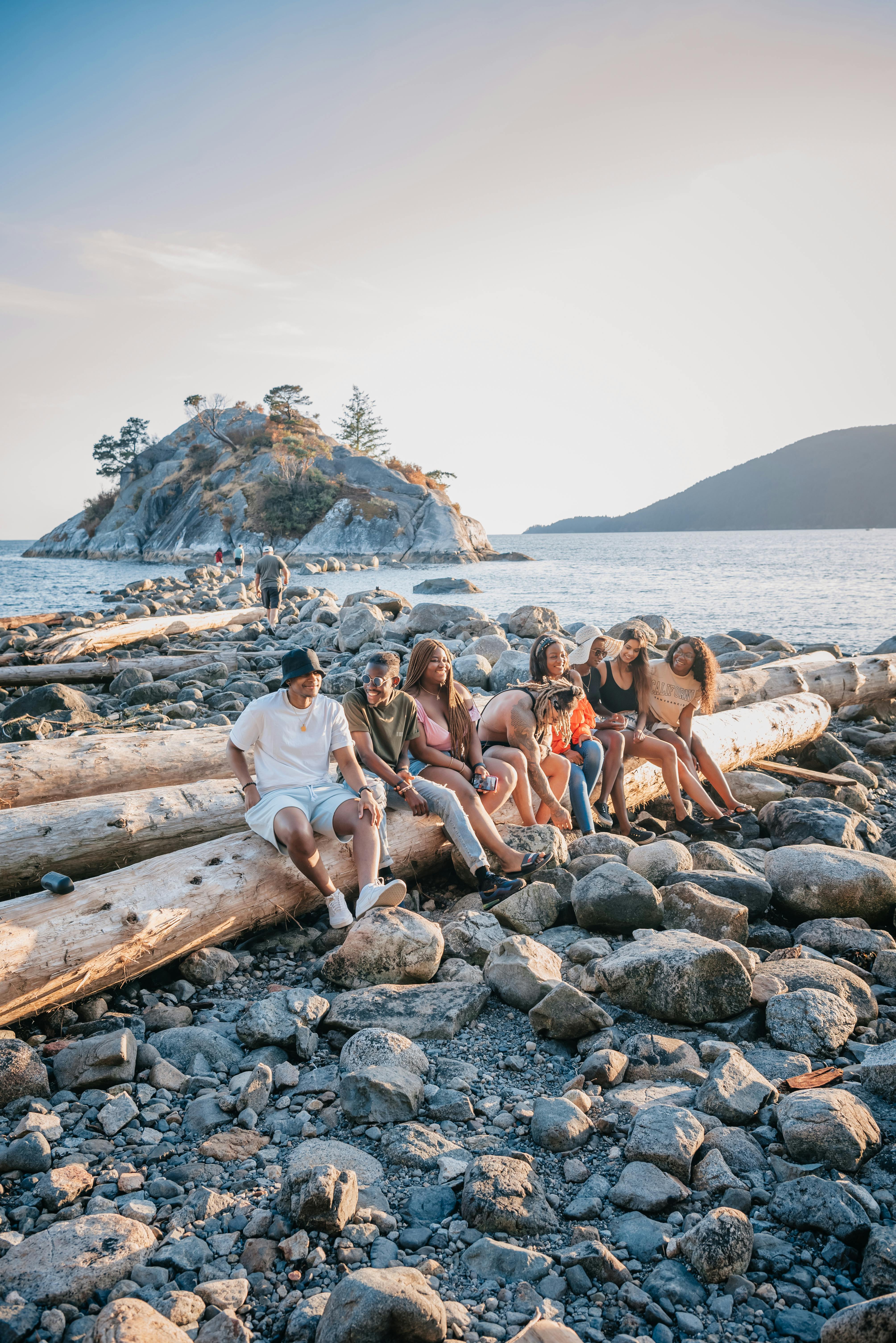 A group of friends sitting on a log at the beach, enjoying a summer day together.