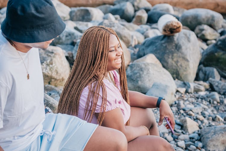 Man And Woman Sitting On A Rocky Beach And Smiling 