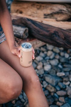 Close-up of a person holding a can with a blurred background, seated on logs.