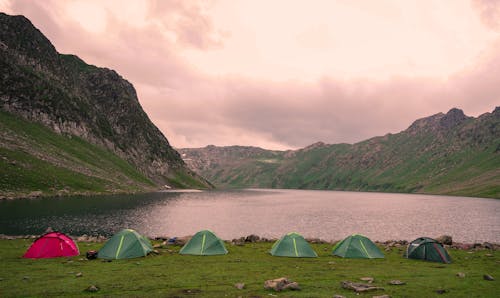 Green Tents on Green Grass Field Near Lake Under Cloudy Sky