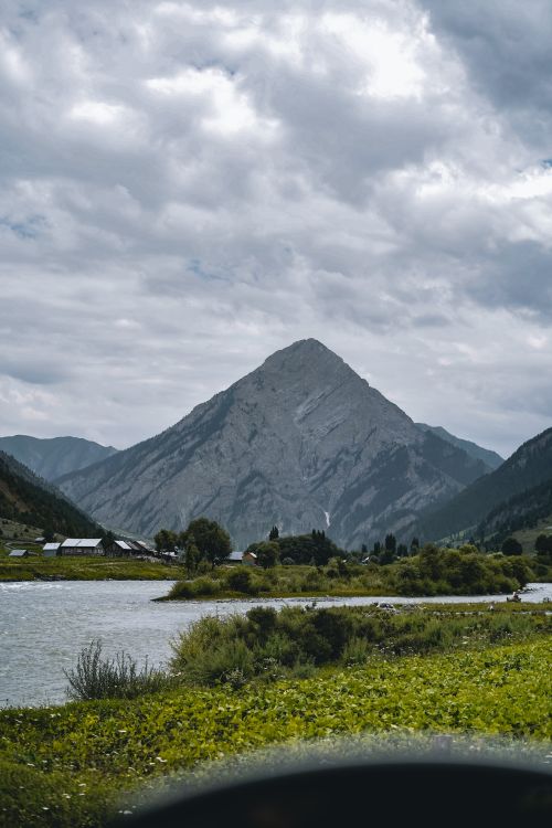 Free Scenic view of a towering mountain surrounded by lush greenery and a gentle river. Stock Photo