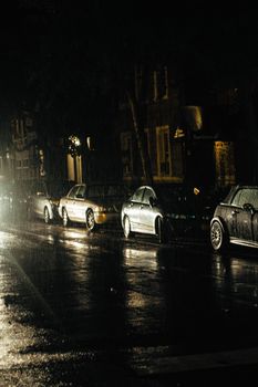 Cars parked in the rain on a dimly lit residential street at night.