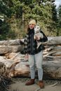 Woman in Black and White Plaid Coat and Blue Denim Jeans Standing on Brown Tree Log