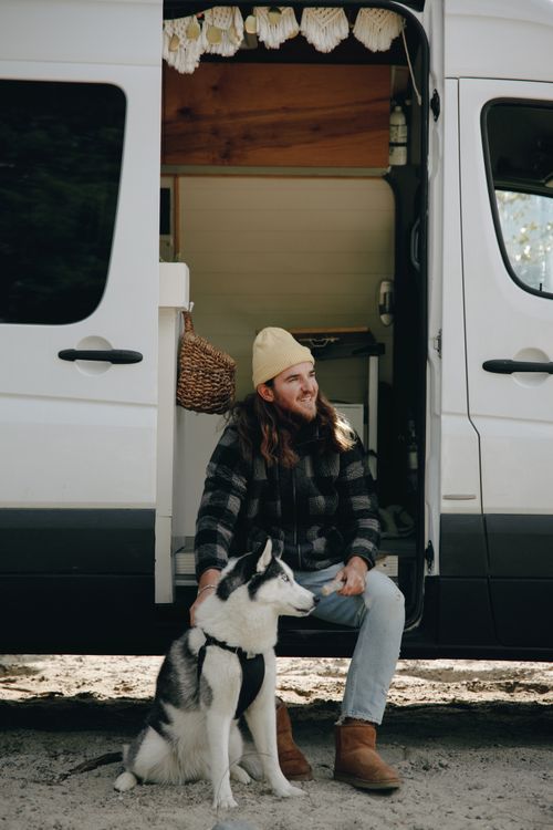 Free A man and his Husky relaxing beside a travel van, enjoying nature. Stock Photo