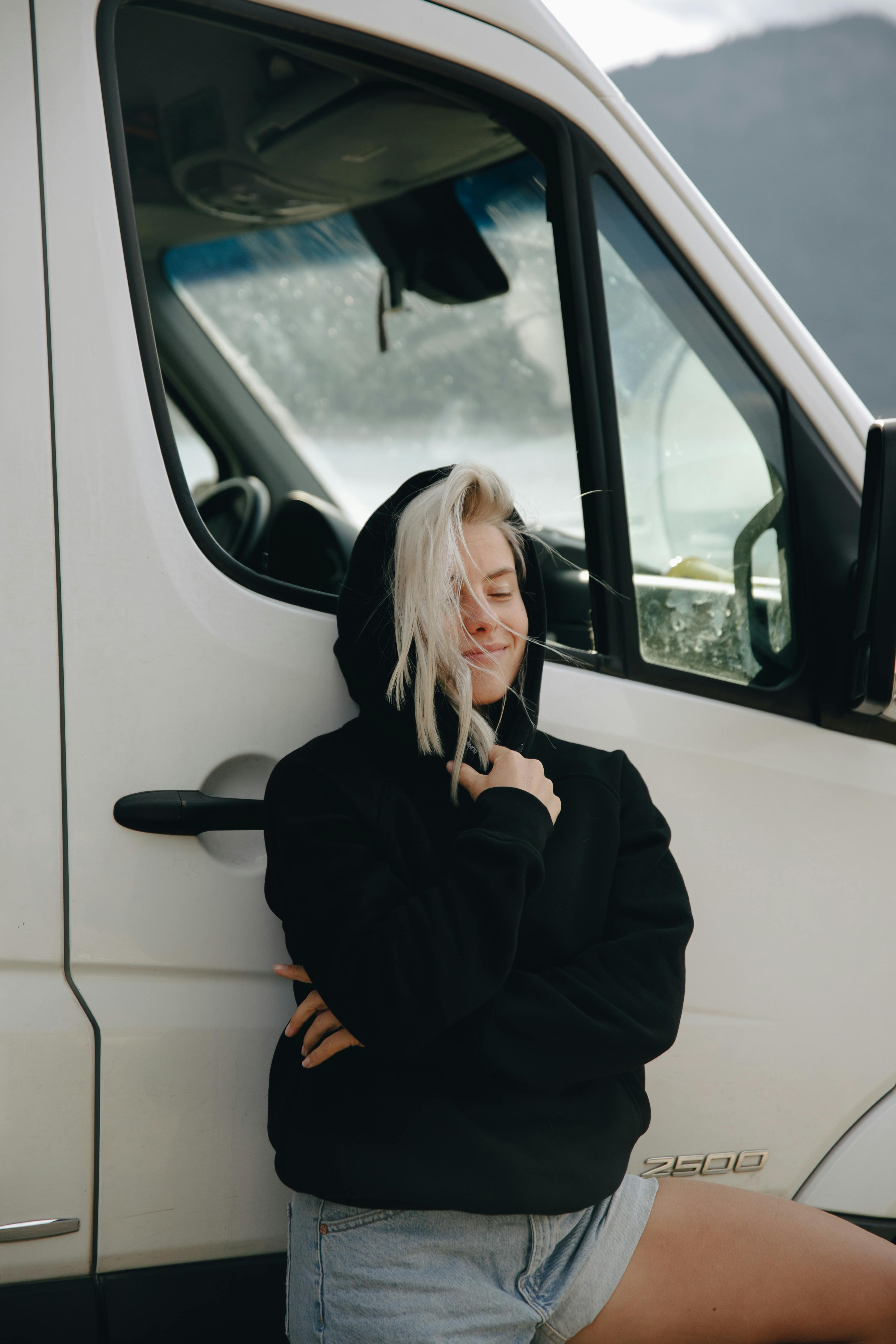 woman in black hoodie leaning against a van