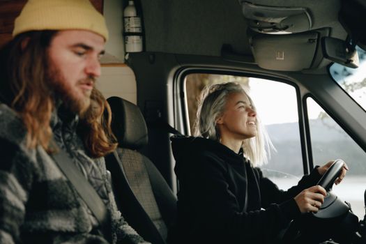 A young couple road-tripping in a camper van. The woman drives while the man relaxes.