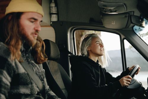 Free A young couple road-tripping in a camper van. The woman drives while the man relaxes. Stock Photo