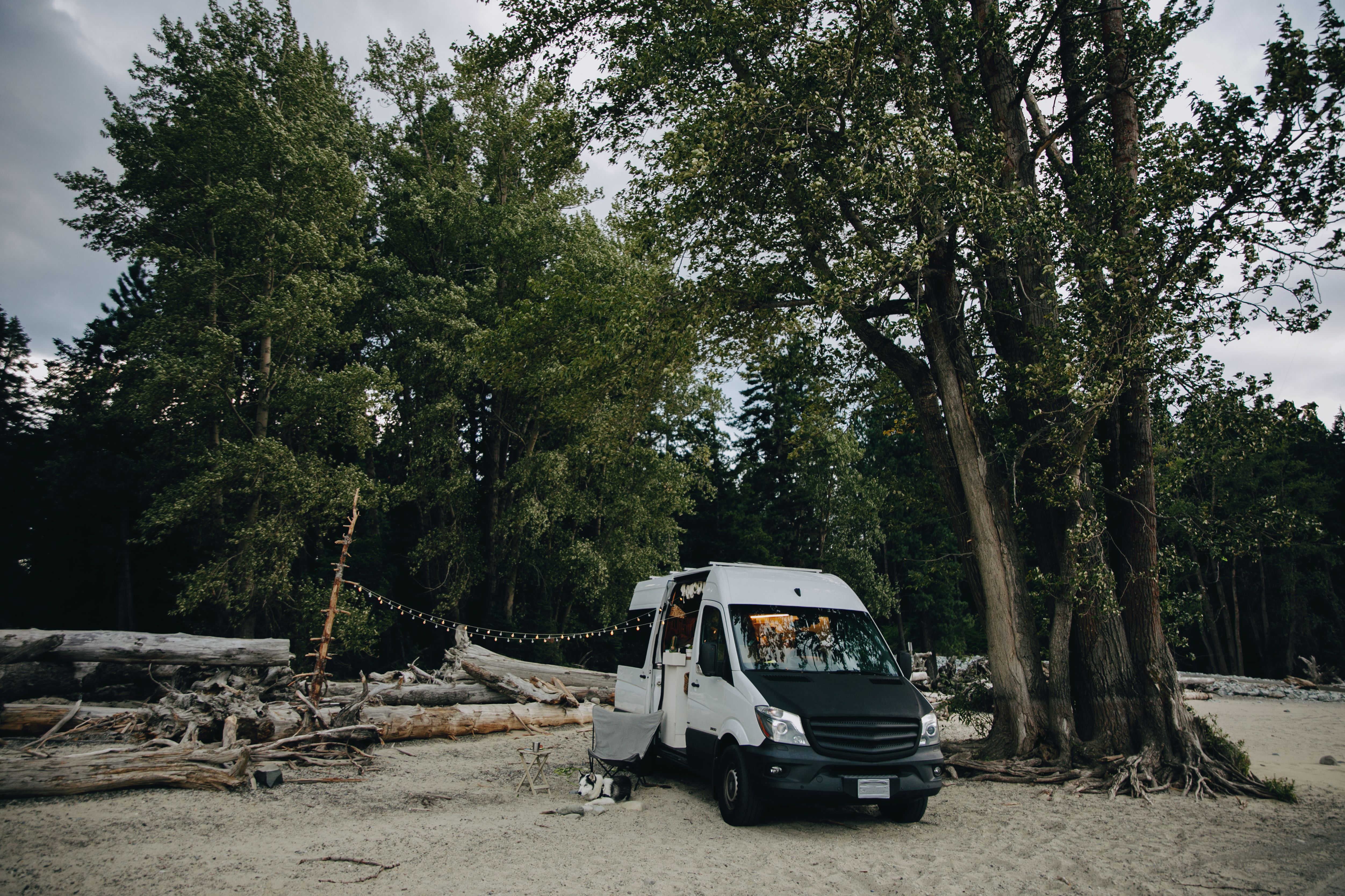 A cozy camper van parked by the forest edge on a serene sandy beach, perfect for adventurous travelers.