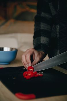 Close-up of a person slicing ripe tomatoes on a black chopping board indoors.