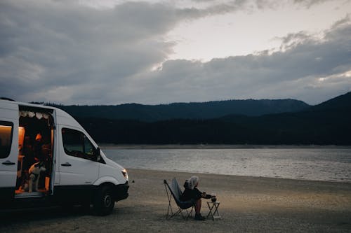 Woman Sitting on a Folding Chair on a Beach near a Campervan 