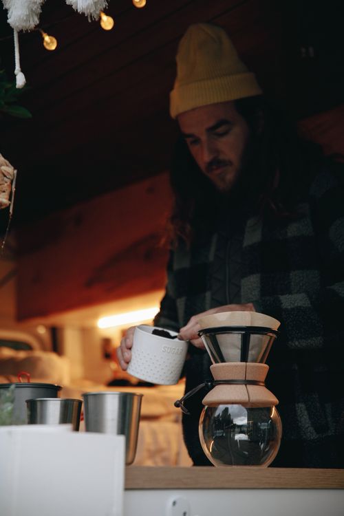 Free A man in a beanie brews coffee using a pour-over method indoors. Stock Photo