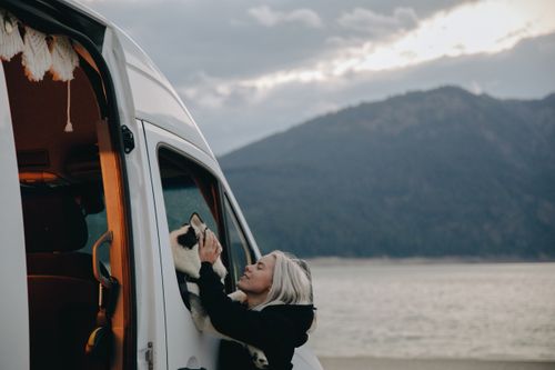 Free Blonde woman enjoying a moment with her dog by a van at a mountain lake. Stock Photo