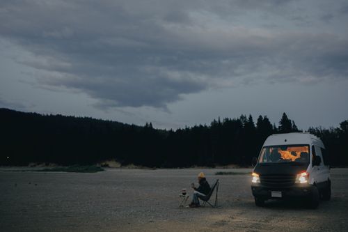 Free Relaxed camping scene at dusk with a solitary van and camper by the forest. Stock Photo