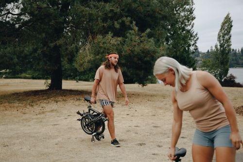 Free A couple in casual attire enjoys an outdoor adventure walking with folding bikes in a park setting. Stock Photo