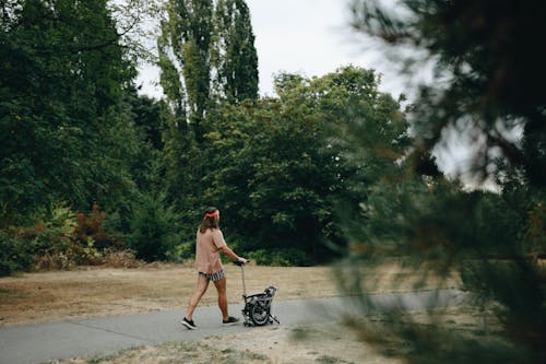 A Man in a Beige Shirt Pushing a Folding Bike on a Road