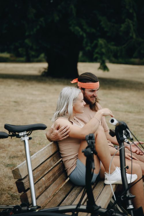 Free Happy couple sitting together on a park bench with bicycles, enjoying a sunny day outdoors. Stock Photo