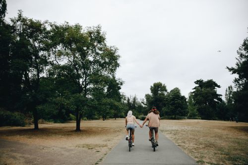 Free Couple riding bicycles while holding hands in a serene park setting. Stock Photo