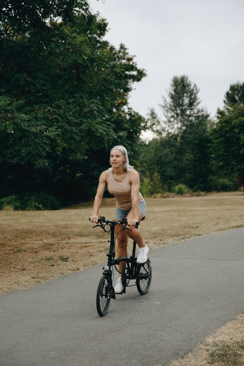 Free A woman cycling through a scenic park on a paved path surrounded by greenery. Stock Photo